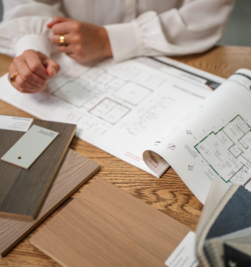 Printed Fowler Homes floor plans spread on a table with timber and fabric samples